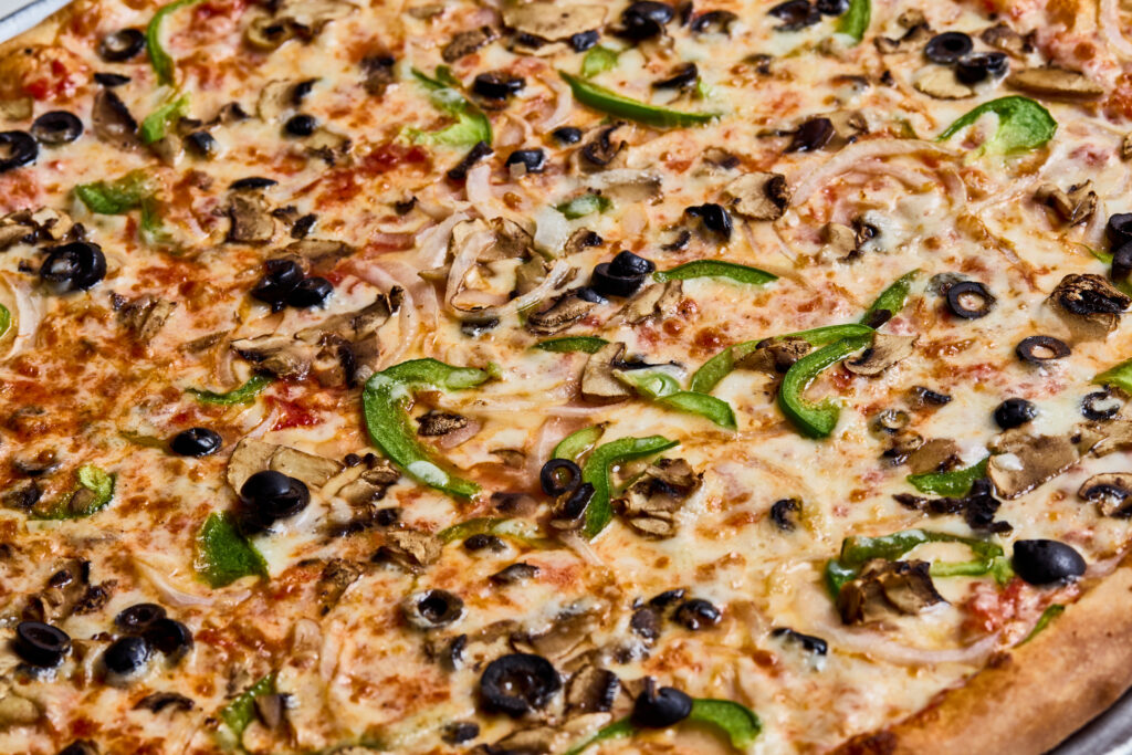 This image shows a vegetable pizza topped with green bell peppers, black olives, mushrooms, onions, and melted cheese. The crust is golden brown, and the toppings are evenly spread over a tomato sauce base.